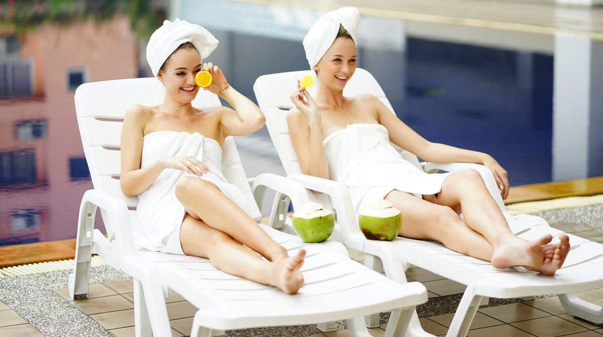 two women relax on the deck chairs with white towel at the swimming pool