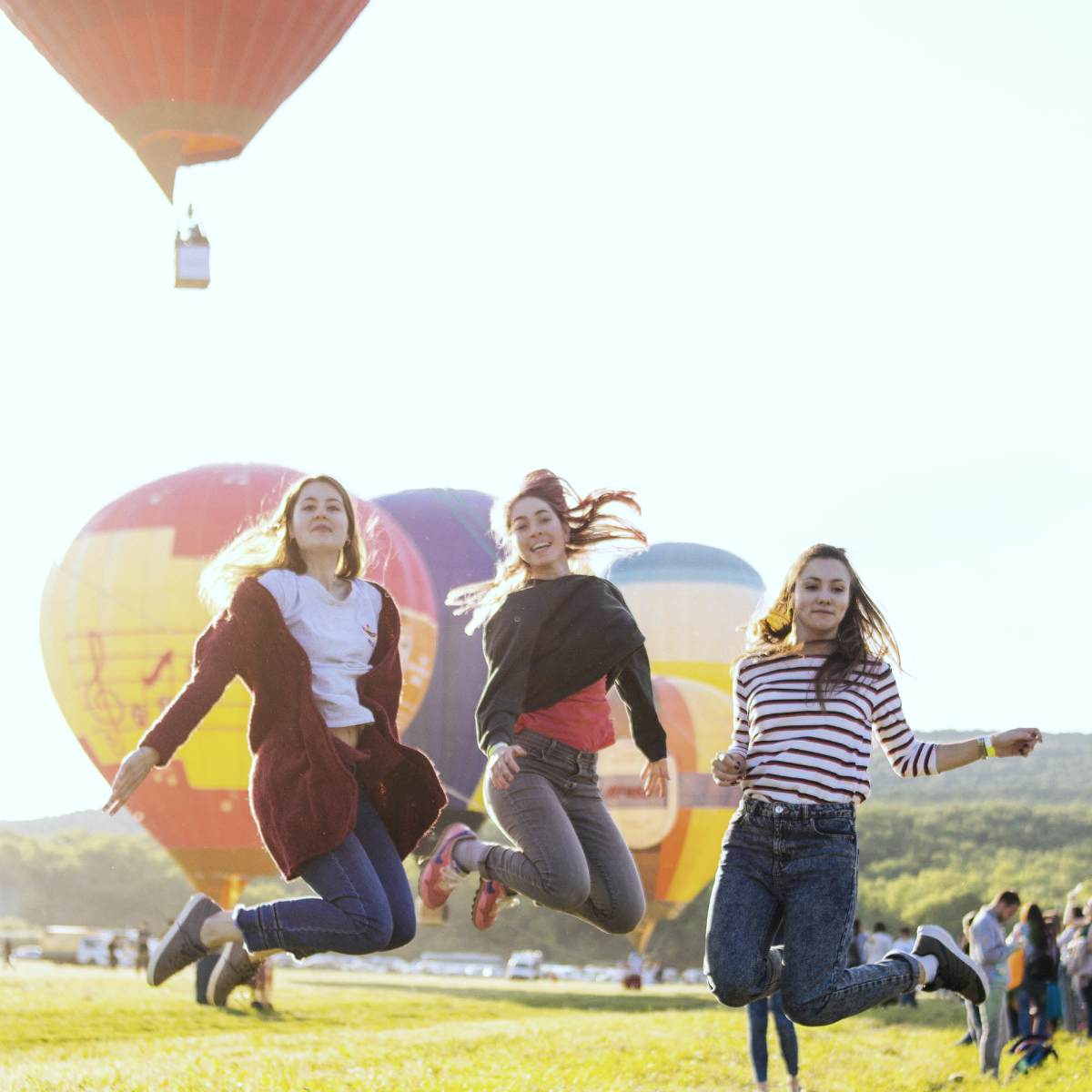 three women jumping above green grass with hot air balloon on the background | Bachelorette Party Ideas For A Weekend Of Wellness [INFOGRAPHIC] | relaxing bachelorette party ideas | classy bachelorette party ideas 