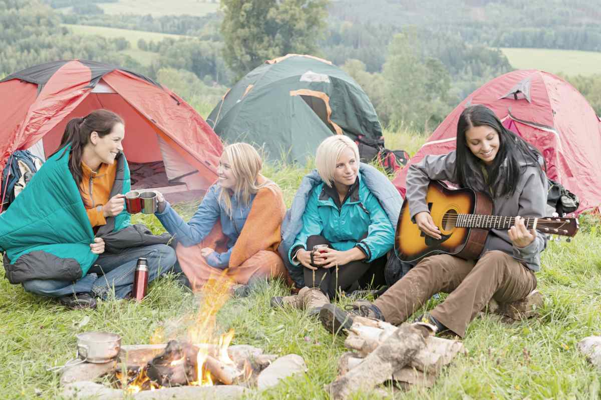 Girls on vacation camping with tents listening to girl playing guitar | Bachelorette Party Ideas For A Weekend Of Wellness [INFOGRAPHIC] | relaxing bachelorette party ideas | classy bachelorette party ideas