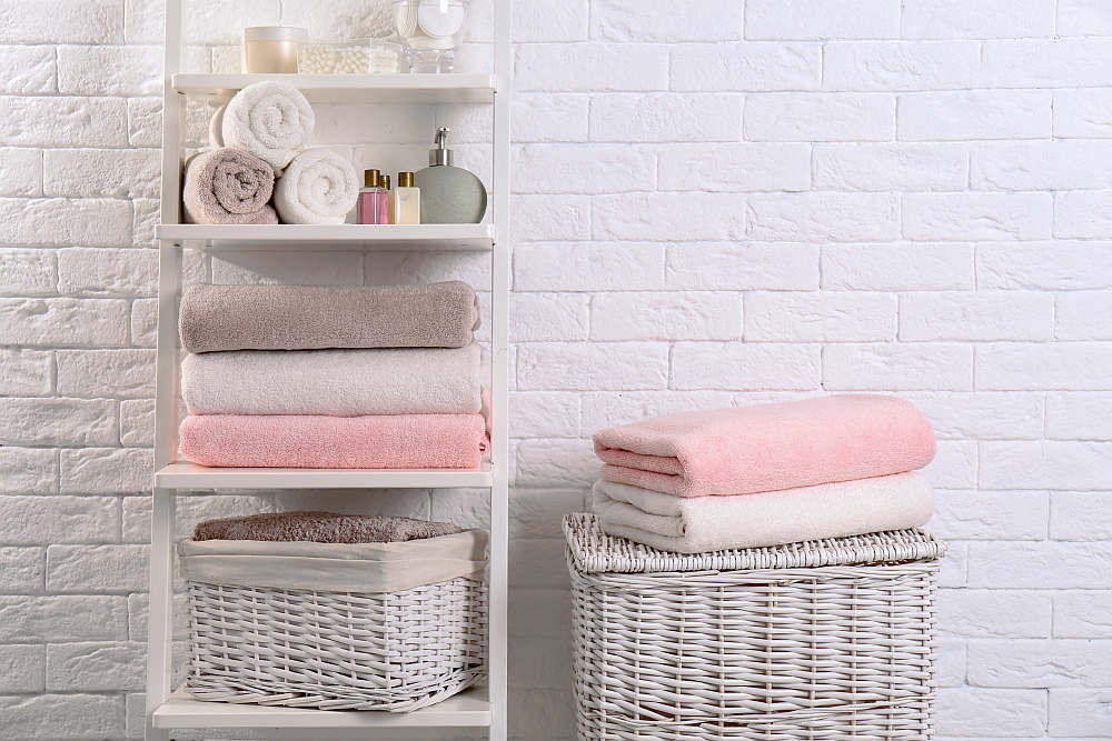 Shelving unit and baskets with clean towels and toiletries near brick wall | How Often Should You Replace Your Airbnb Linens And Towels | how often should you replace your towels | how often should you replace towels