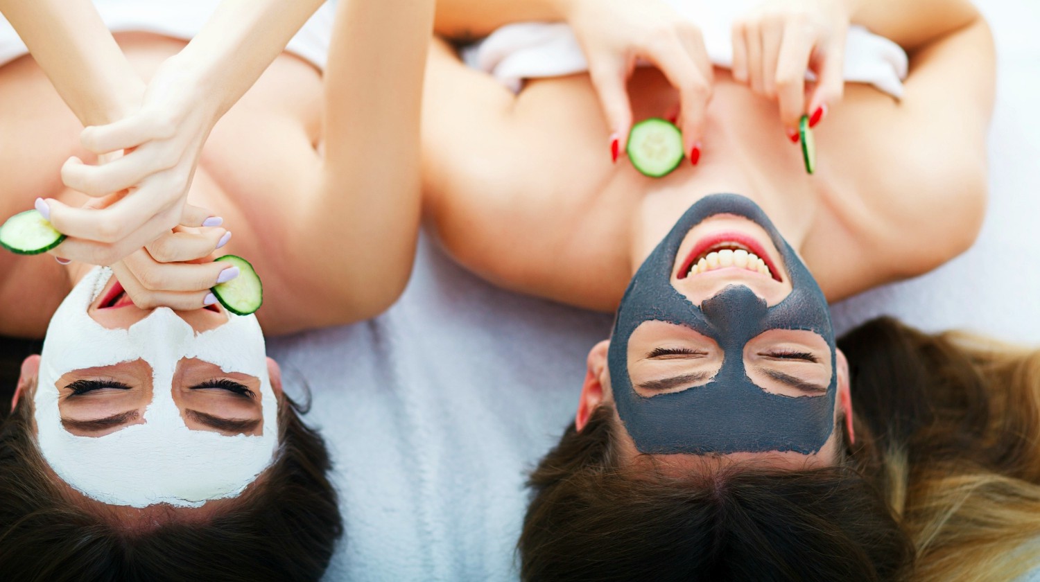 Featured | Two women holding pieces of cucumber on their faces lying the bed | Recipe For A Perfect Girls Night In