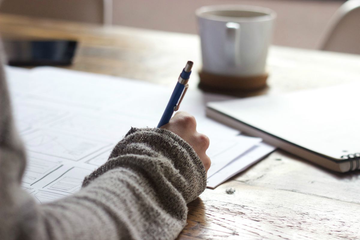 Person writing on brown wooden table near white ceramic mug | Morning Routine Tips To Jumpstart Your Day