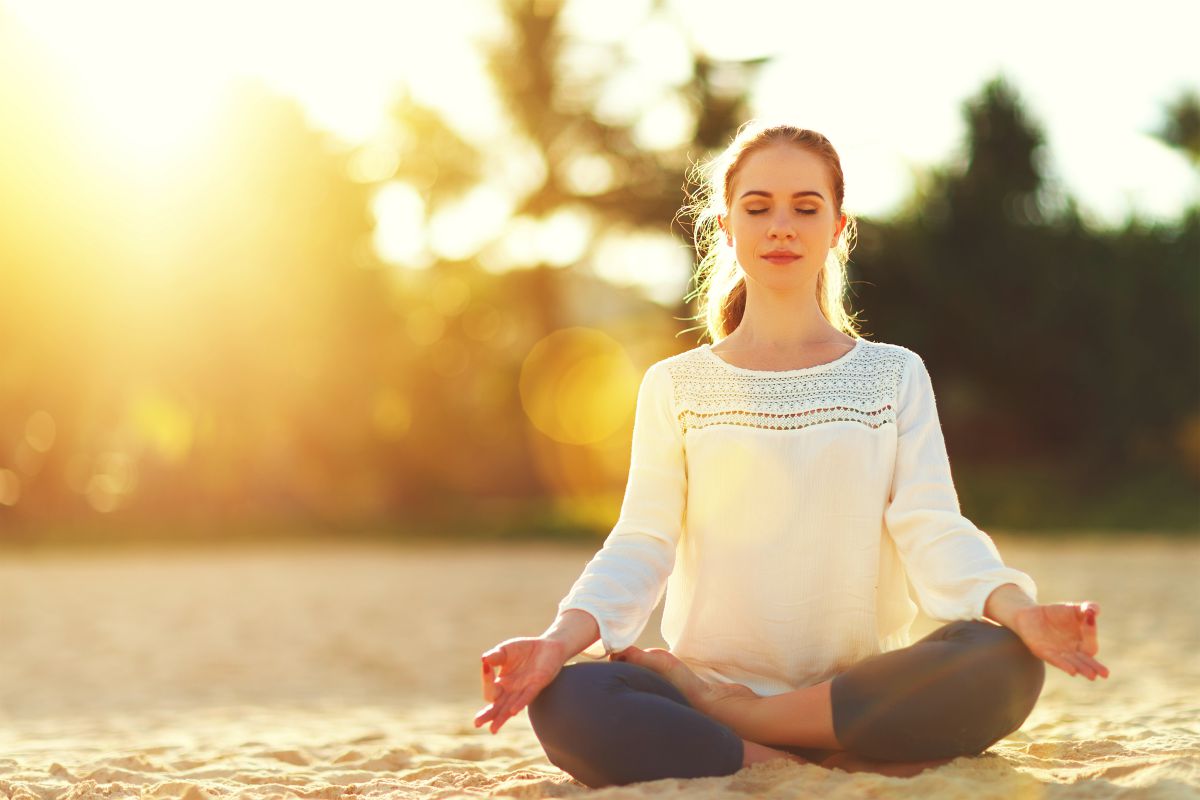 Woman practices yoga and meditates in the lotus position on the beach | Morning Routine Tips To Jumpstart Your Day