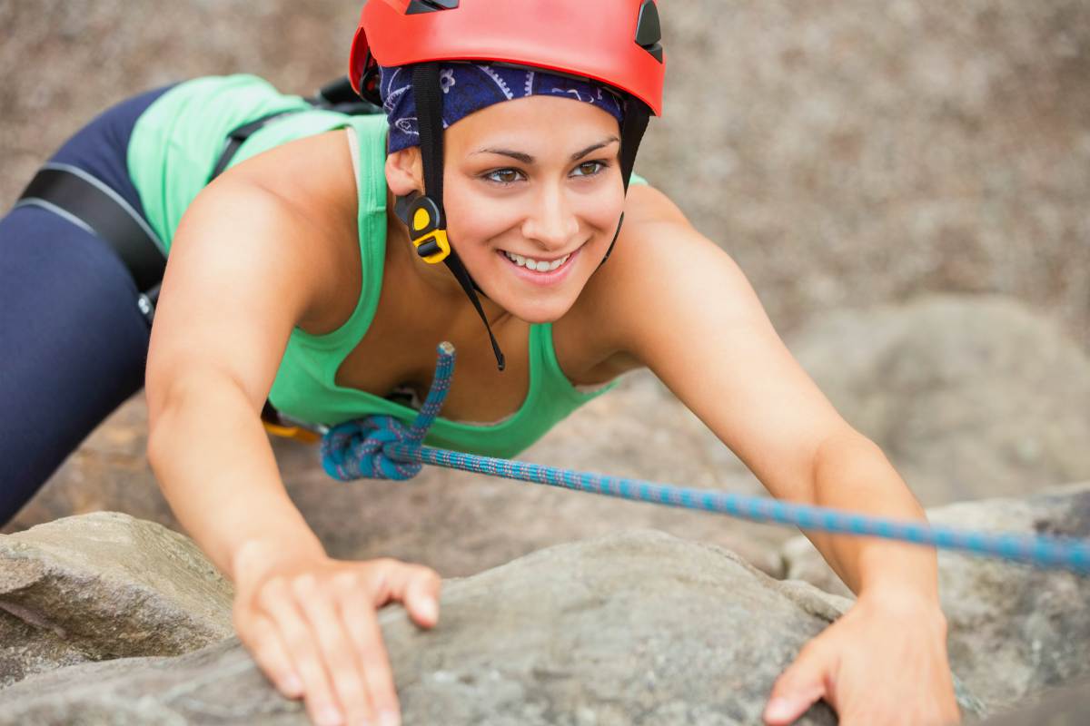 Happy girl climbing rock face wearing red helmet | Bachelorette Party Ideas For A Weekend Of Wellness [INFOGRAPHIC] | relaxing bachelorette party ideas | unconventional bachelorette party ideas