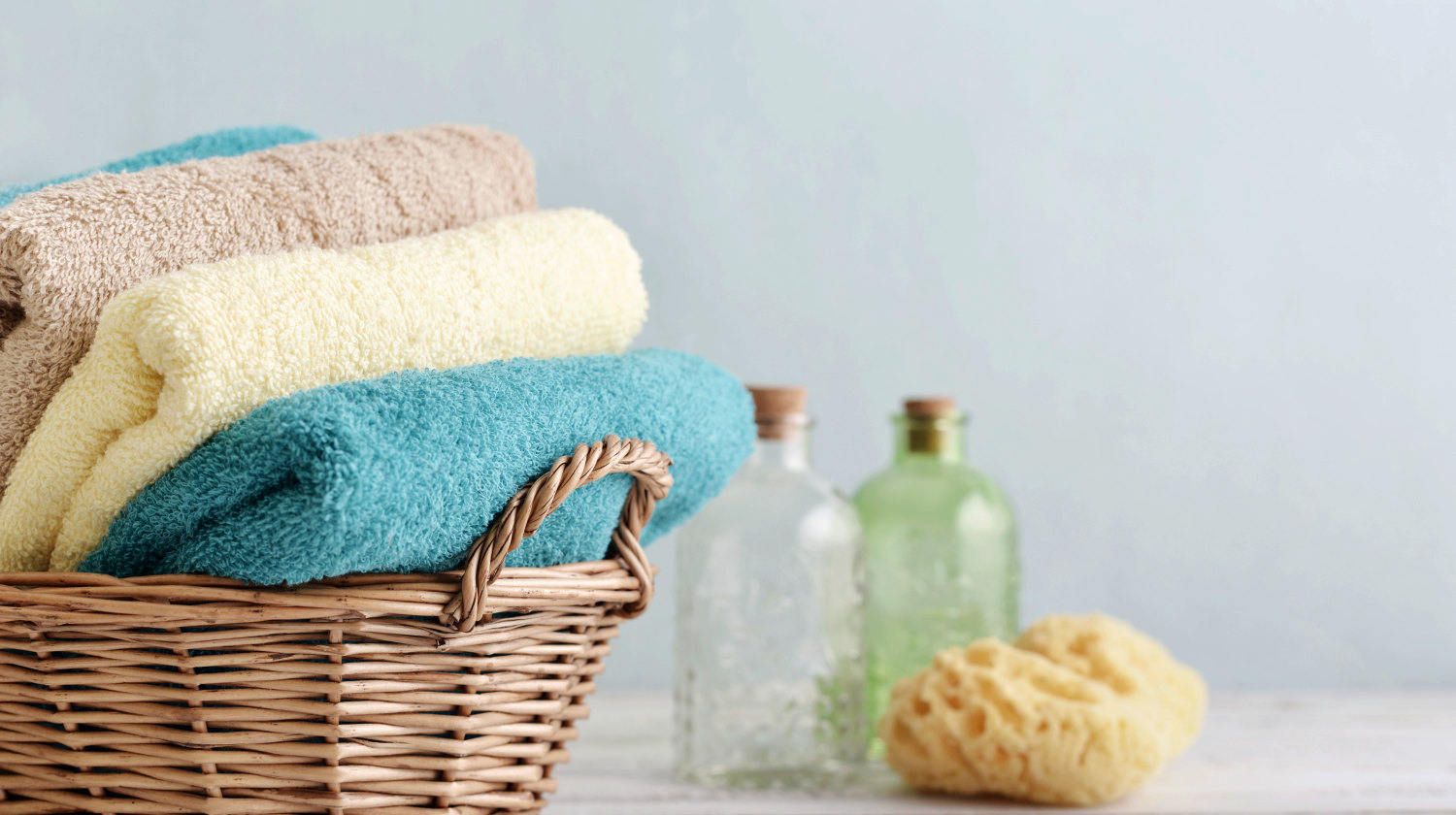 Feature | Bath towels of different colors in wicker basket on light background | How To Get Sour Smell Out Of Towels