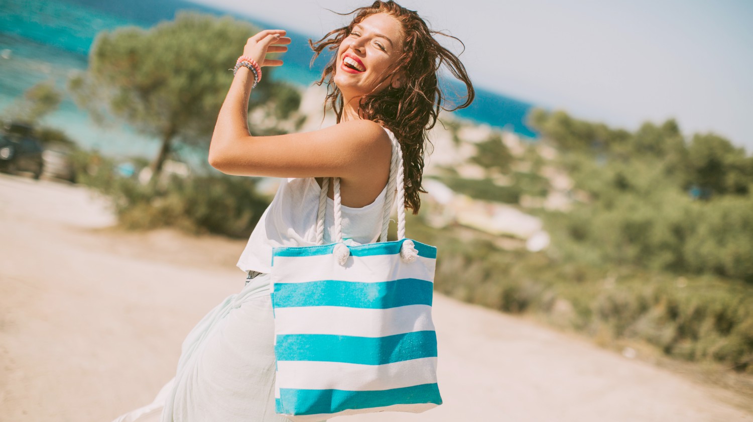 Featured | happy woman with bag | Beach Essentials You Shouldn’t Be Without On Your Next Trip | beach bag essentials