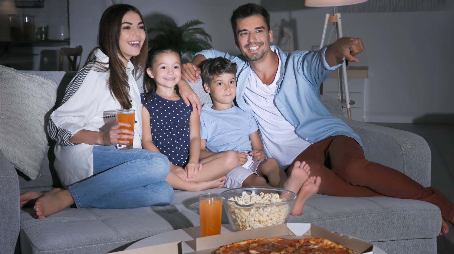Happy family watching TV on sofa at night | Ways to Make Family Movie Night Even More Fun | movie night | movie night ideas | Featured