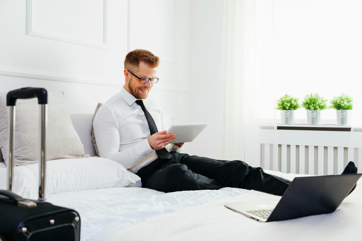 young businessman on bed working tablet | Ways To Be The Best Bed And Breakfast Host | best bed and breakfast | bed and breakfast.com reviews
