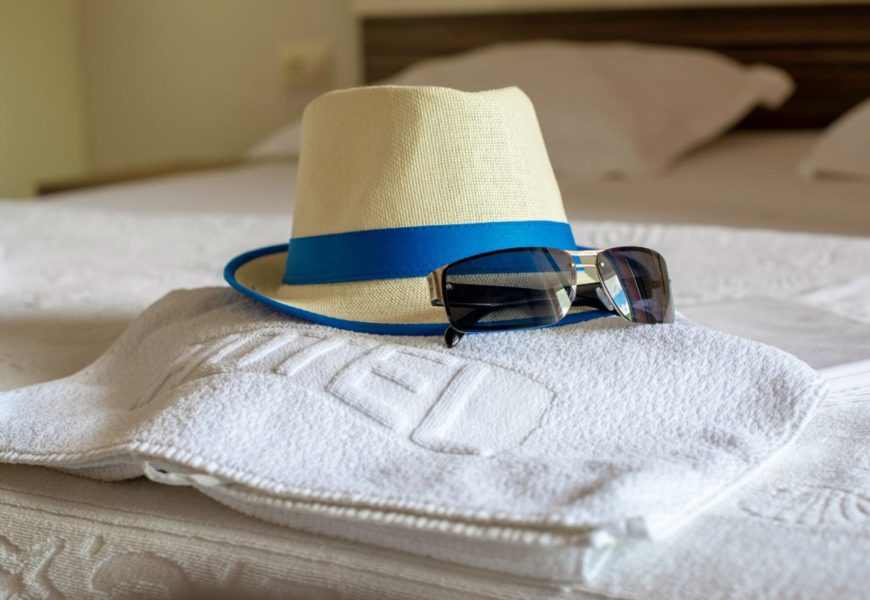 hat towel and sunglasses on bed | Advantages Of Using Personalized Beach Towels To Promote Business | beach towels | custom beach towels | Featured