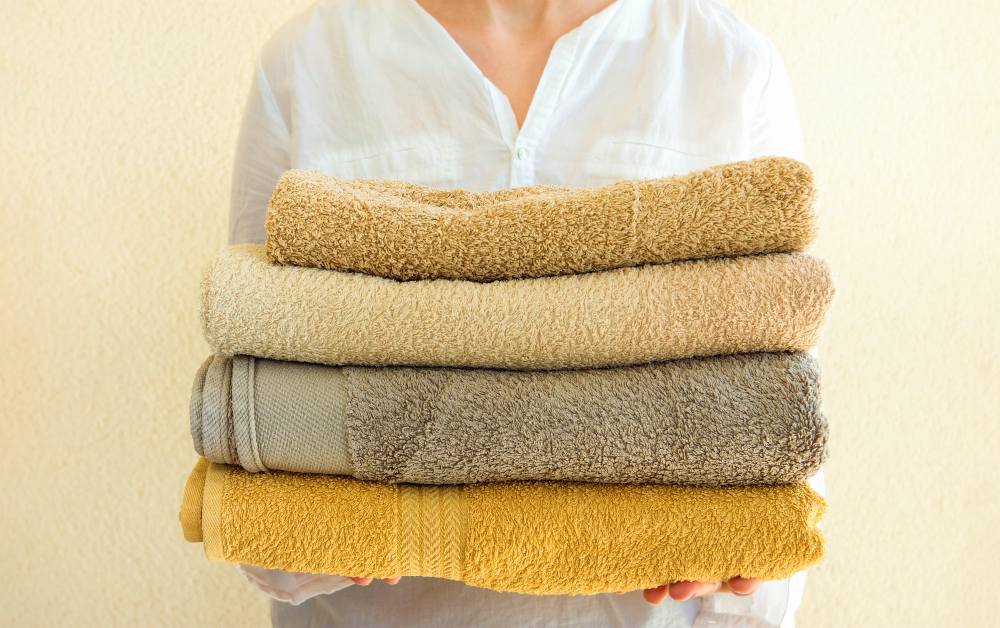 Young caucasian woman holds in hands stack of clean folded terry towels | How To Choose The Best Luxury Bath Towels | luxury towels | luxury towels