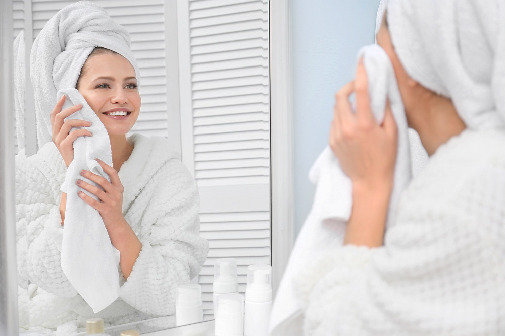 Young woman wiping her face with towel in bathroom | How To Choose The Best Luxury Bath Towels | luxury towels | luxury bath towels