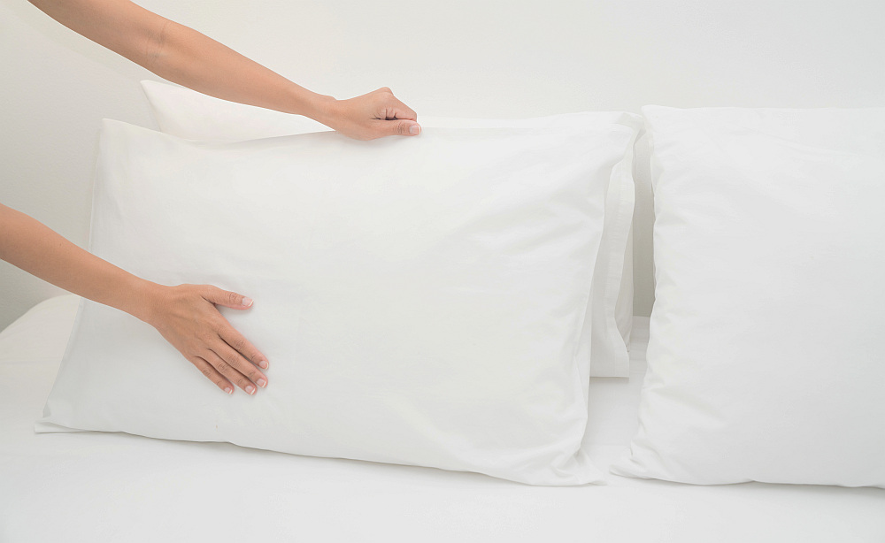 Hand set up white pillow on bed sheet in a room | How Often Should You Replace Your Airbnb Linens And Towels | how often should you replace your towels | how often replace towels