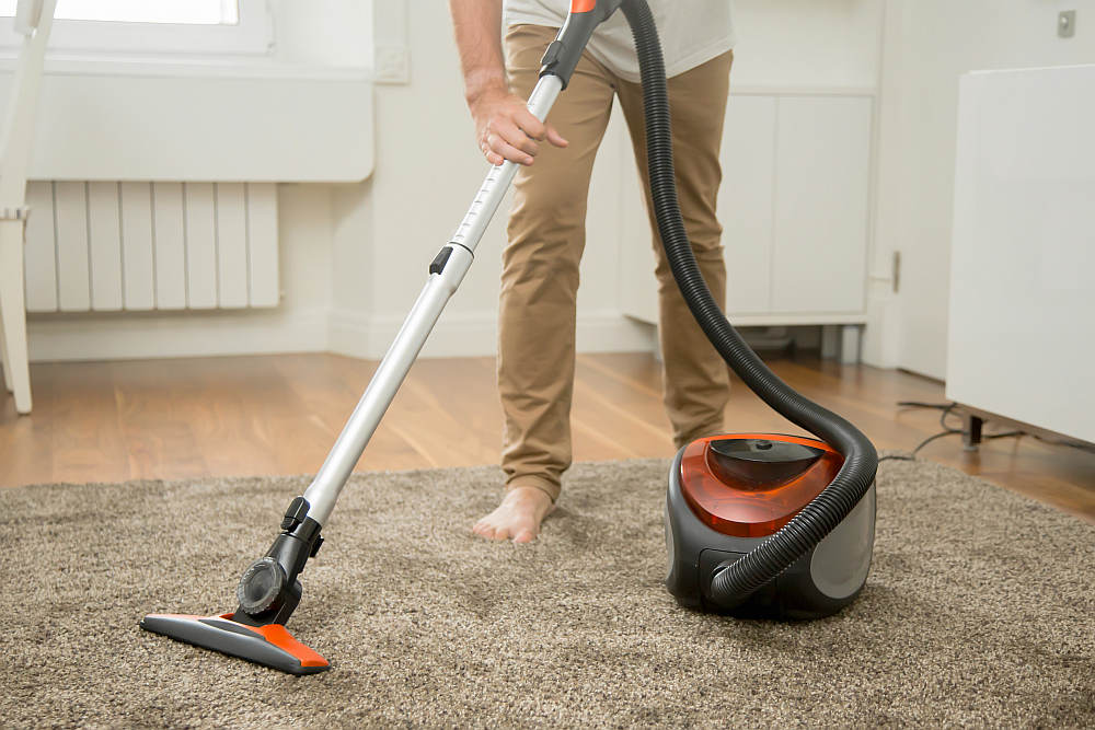 Man vacuum cleaning the carpet in the living room | How Often Should You Replace Your Airbnb Linens And Towels | how often should you replace your towels | mattress