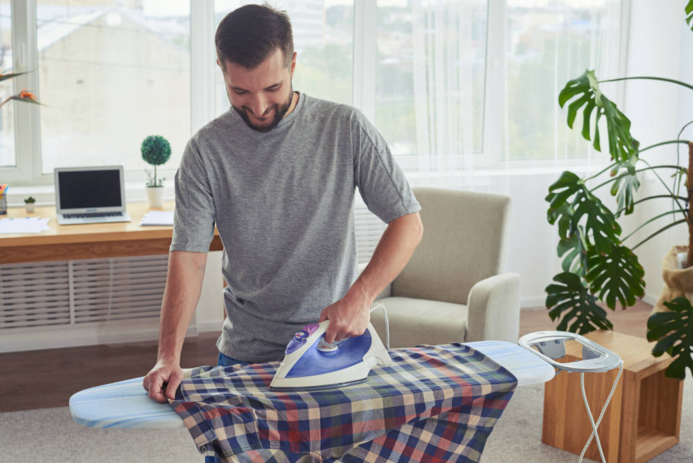 Man with charming smile ironing diligently shirt on ironing board | Complete Supplies Checklist For Any AirBnb Host To Gain Satisfied Guests | airbnb host requirements