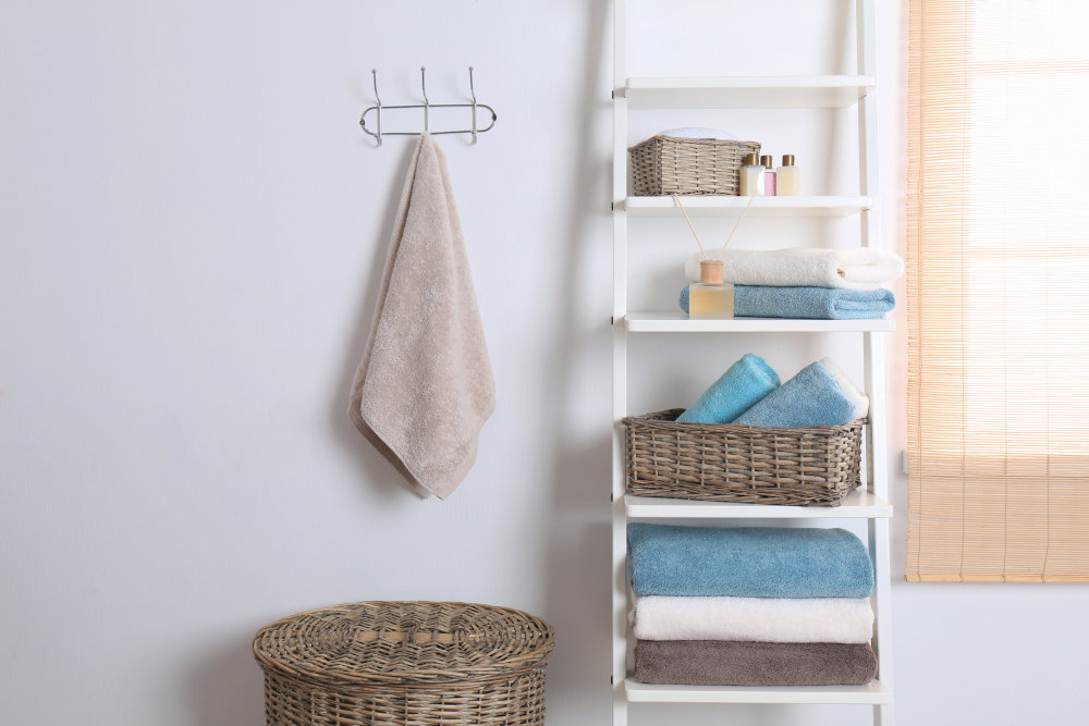 Shelving unit and rack with clean towels and toiletries near white wall | Airbnb Bathroom Essentials To Stock For Your Guests | airbnb amenities