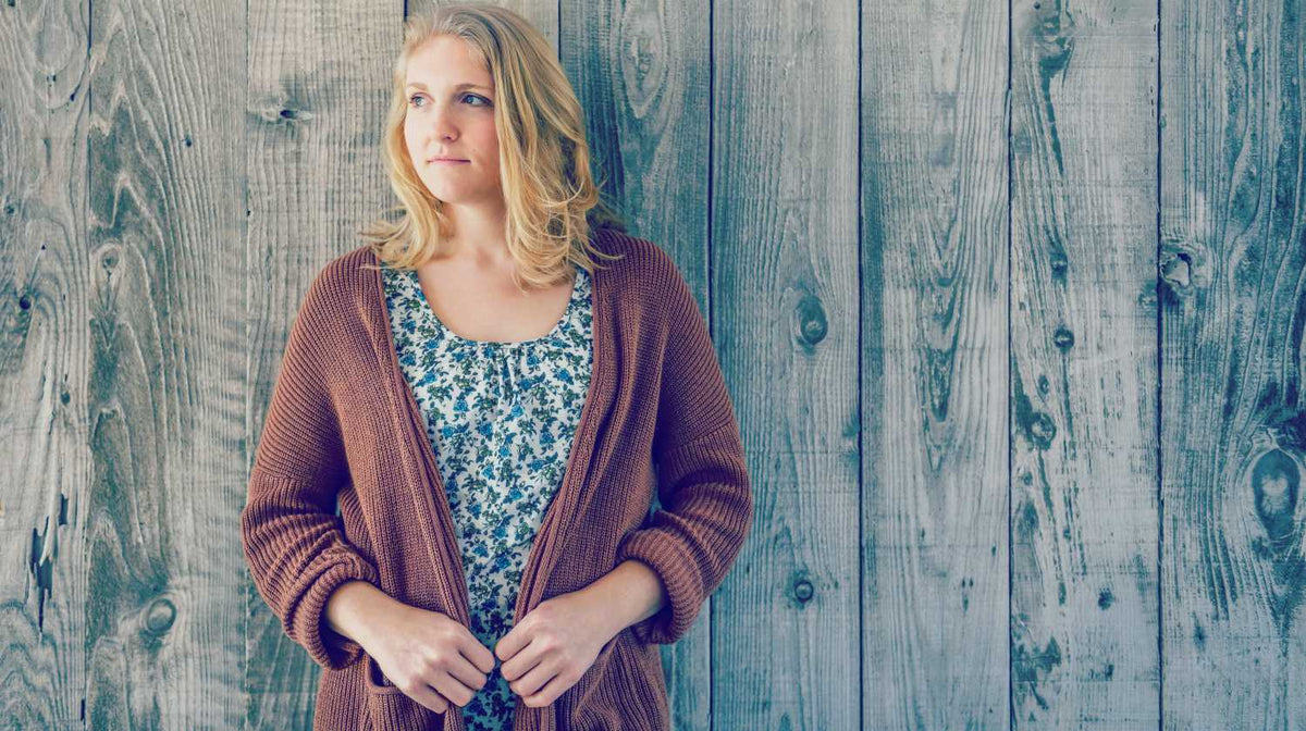woman wearing brown cardigan leaning on wooden wall